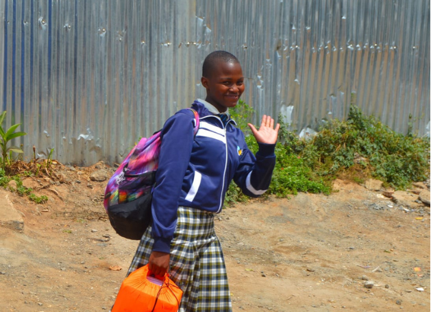 A KGSA student waving while walking to school with her backpack