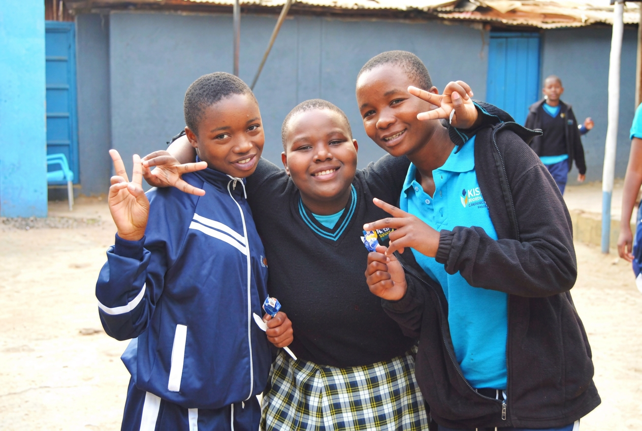 Three KGSA students smiling and making peace signs in the schoolyard
